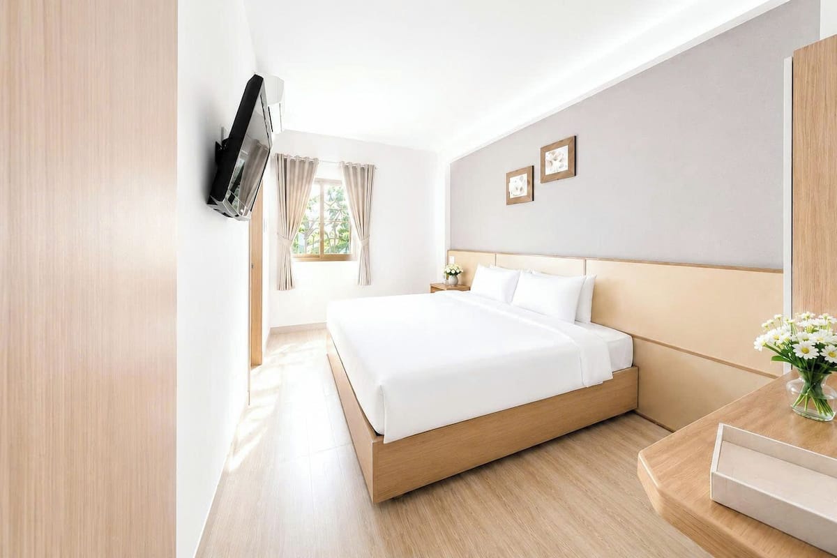 Une chambre d’hôtel avec un lit, un téléviseur fixé au mur, une table de chevet et une fenêtre avec des rideaux.