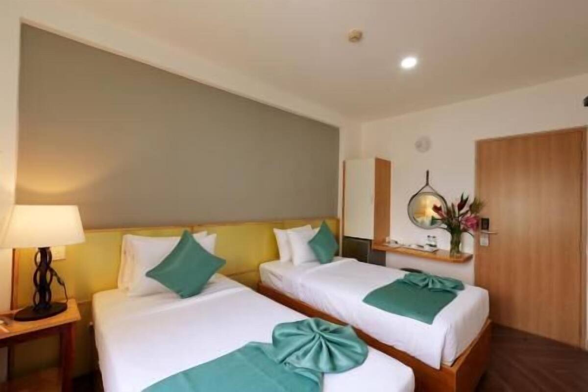 Une chambre d’hôtel avec deux lits, une table de chevet avec une lampe, un miroir et une armoire en bois.