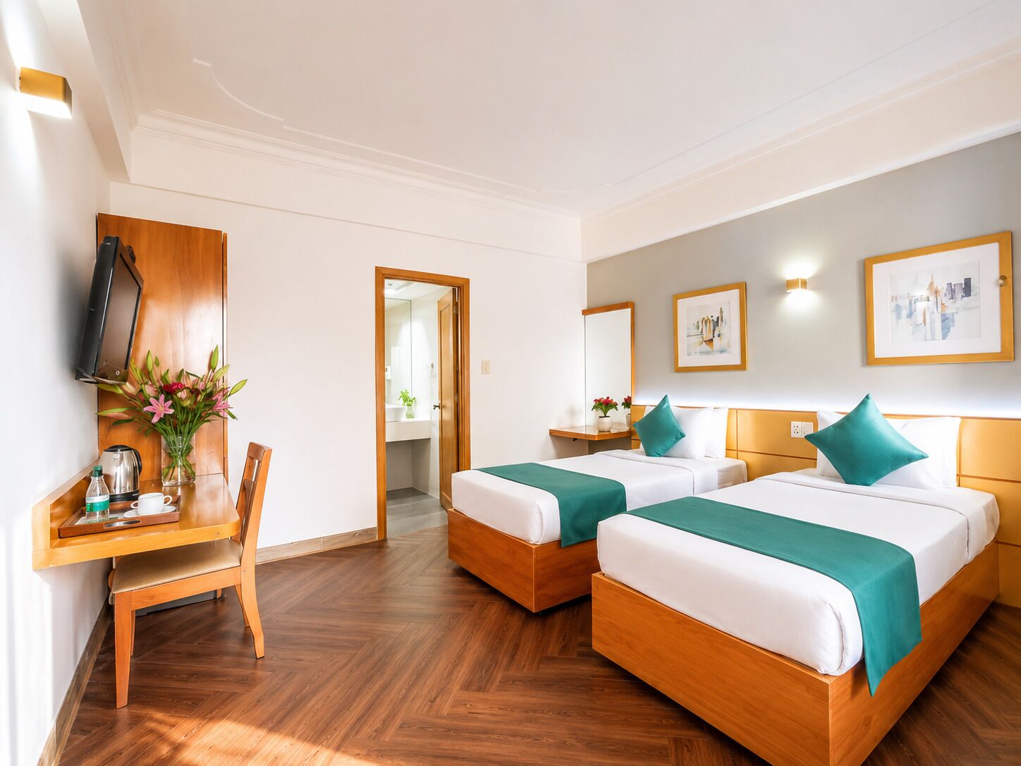 Quarto de hotel com duas camas, uma escrivaninha, uma cadeira, televisão e obras de arte nas paredes.