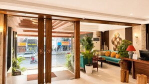 Eine Hotelhalle mit Glastür, einer Sofagruppe, einem Fernseher und einer Rezeption.