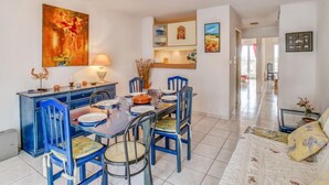 Un coin repas avec une table dressée pour six personnes, des chaises bleues, un buffet bleu et un tableau accroché au mur.