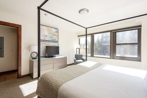 Une chambre avec un grand lit, un téléviseur posé sur une commode et un fauteuil.