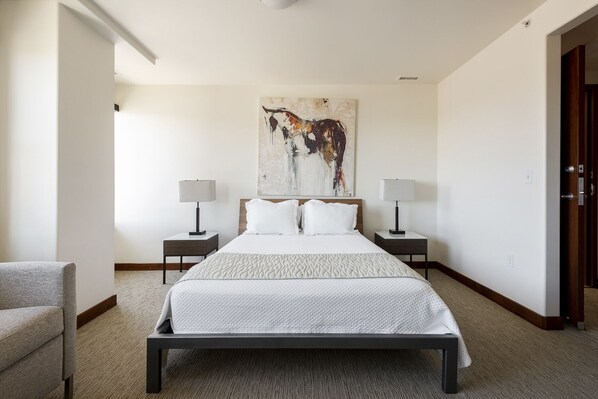 Una camera d'albergo con un letto grande, due comodini con lampade, un quadro astratto di grandi dimensioni sulla parete e una sedia.