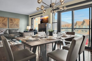 A modern dining area with a large table set for four, a sofa, and a television mounted on the wall. - Ski-In/Ski-Out|Heated Pool and Hot Tub|Fireplace|Managed by Park City Lodging (Park City)