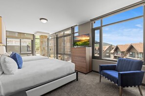 Habitación de hotel con cama, una silla, televisor y ventanas amplias que ofrecen vistas al exterior.
