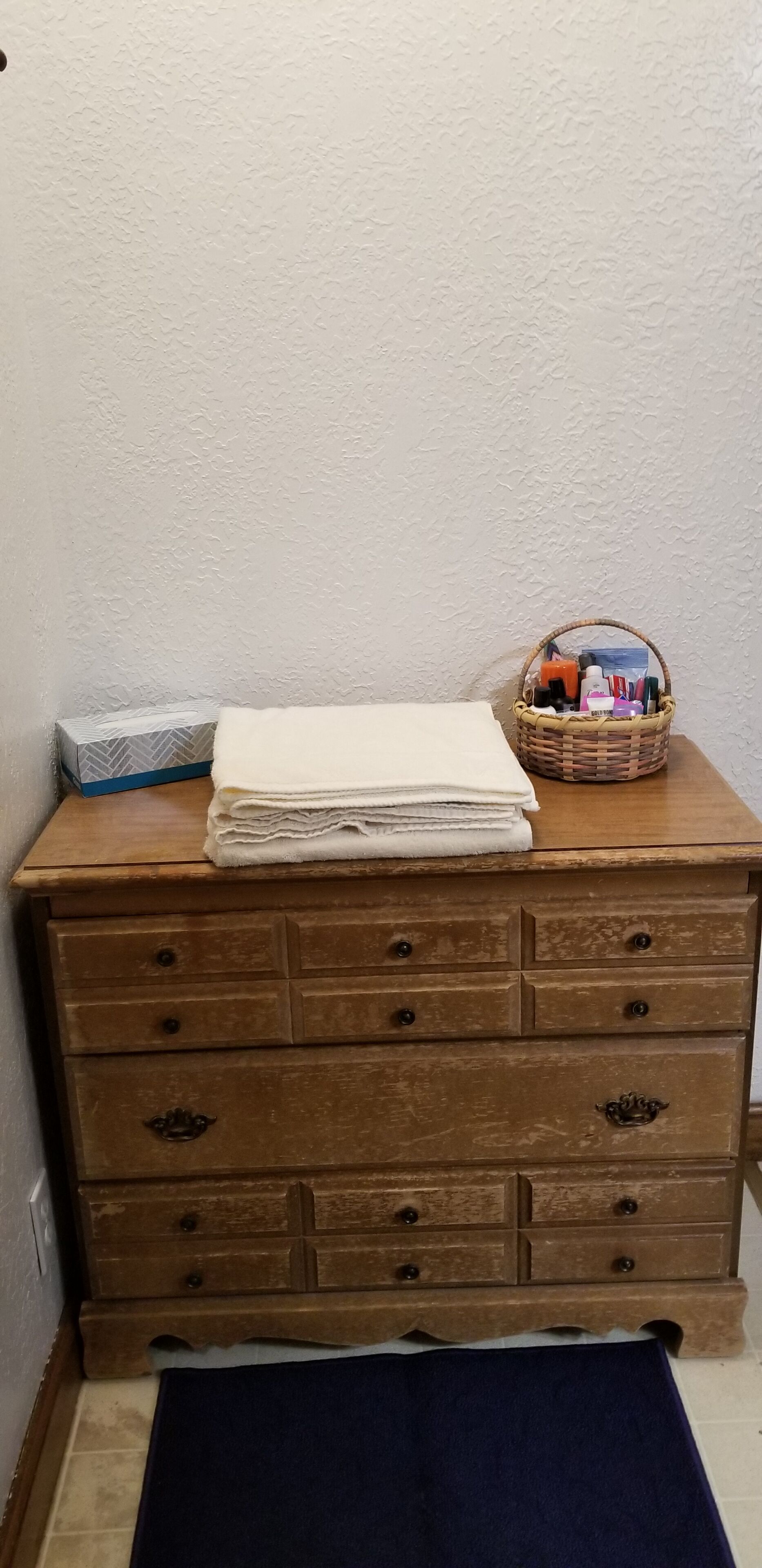 A wooden dresser with a white box and a basket of toiletries.