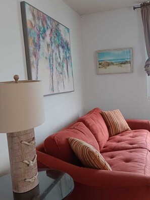 Una sala de estar con un sofá rojo, una lámpara y dos cuadros en la pared.