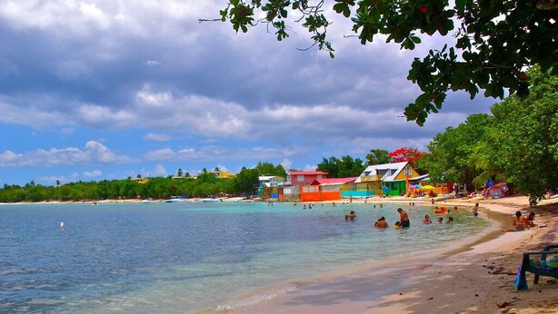 A beach with clear turquoise water, a sandy shore, and colorful buildings in the background. - Spectacular Ocean View  Penthouse, Terrace, 2br, 2bth -  Surrounded by Nature (Cabo Rojo)