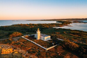 A lighthouse with a white tower and a small adjacent building, surrounded by a fenced area and natural landscape.