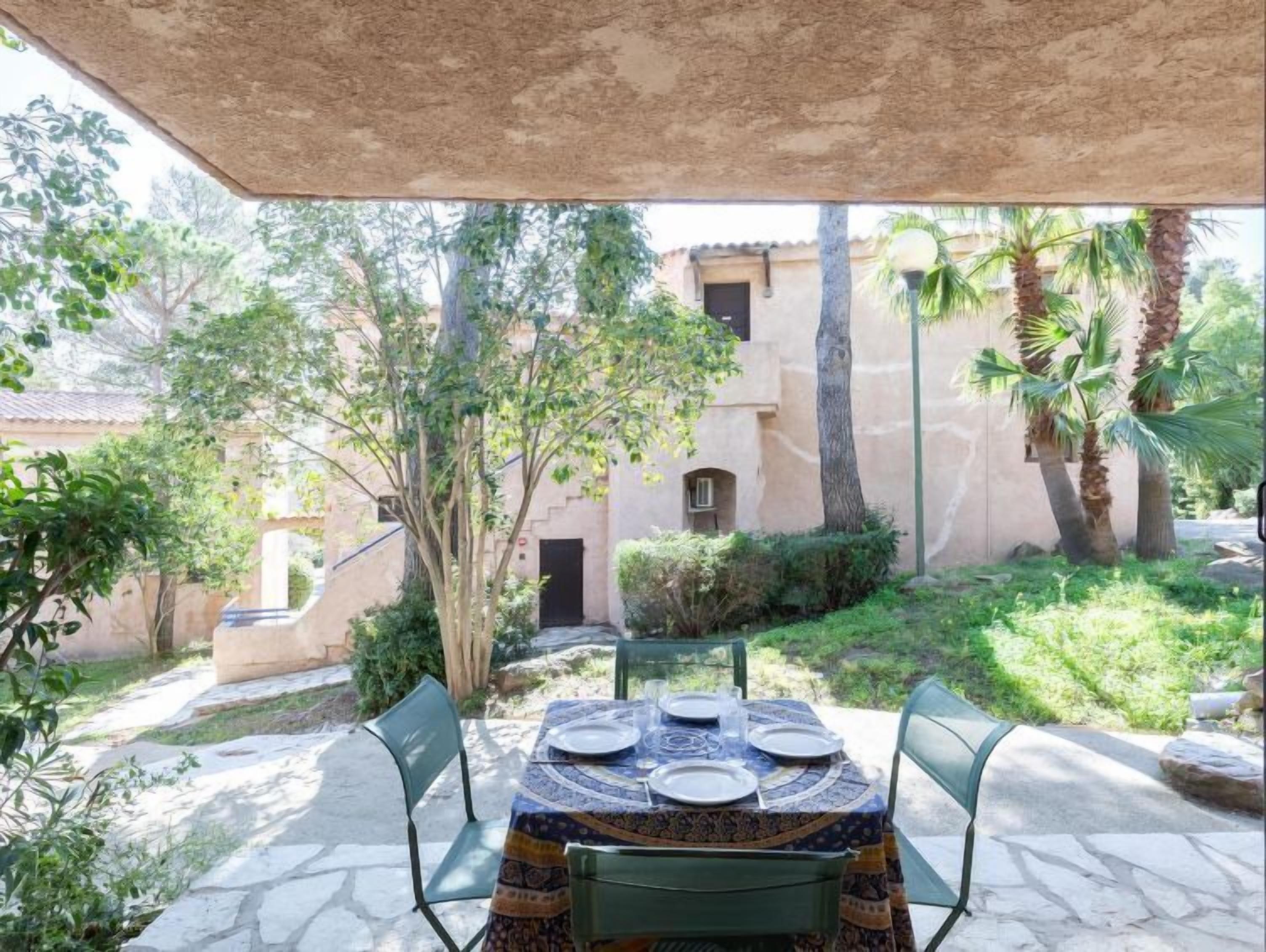 An outdoor patio with a table set for four, surrounded by stone flooring and greenery.