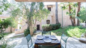 An outdoor patio with a table set for four, surrounded by stone flooring and greenery. - Résidence Les Jardins d'Azur by Interhome (Saint-Raphaël)