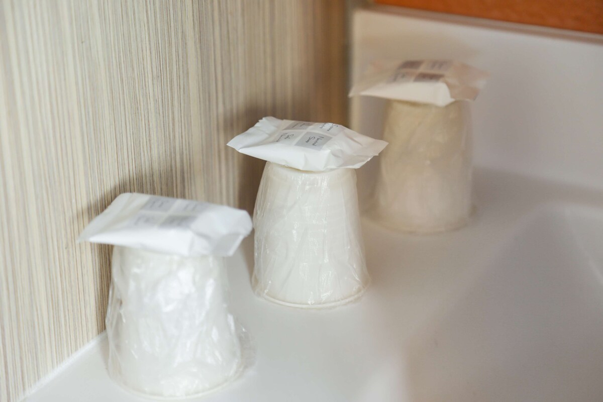 Trois objets cylindriques blancs, enveloppés de plastique, sont posés sur une surface blanche, le tout se détachant sur un fond à rayures.