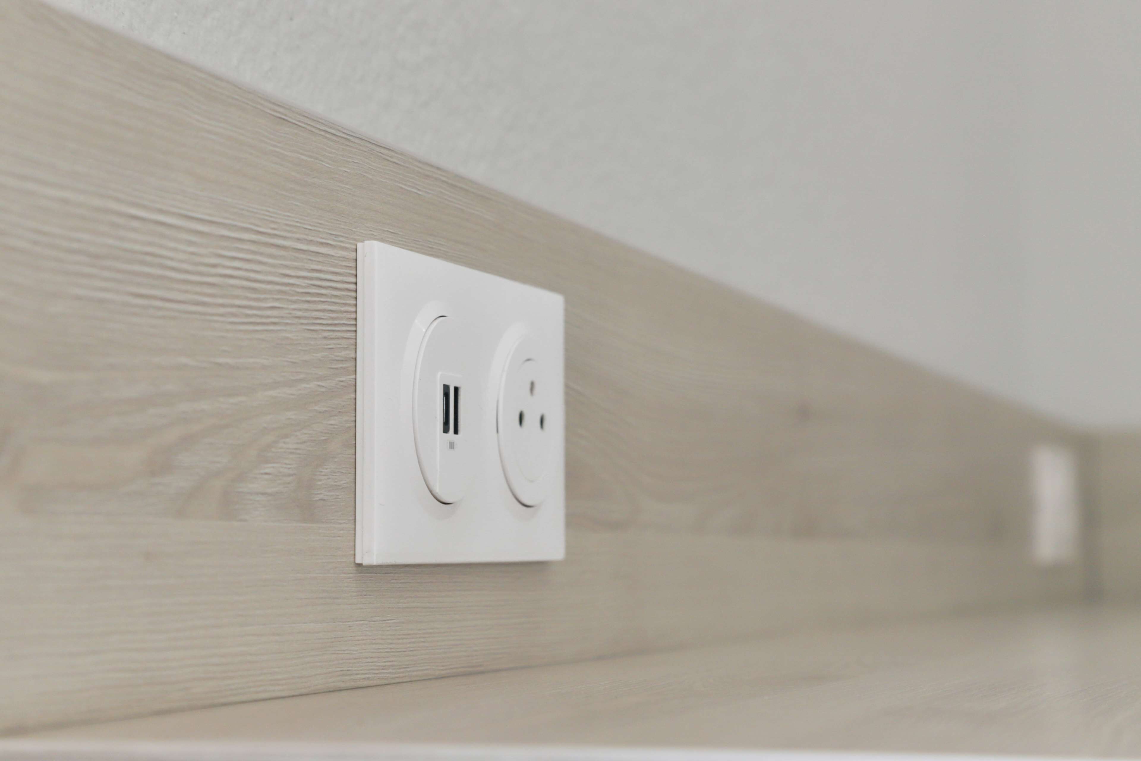 A white electrical outlet on a wall with a wooden panel design.