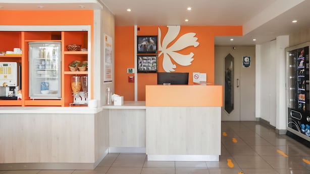 Een receptie met een balie, een koelkast vol drankjes en een decoratief object aan de muur.