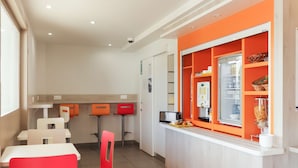 Een modern café met witte en oranje inrichting, met een toonbank met een koffieapparaat en een koelkast.