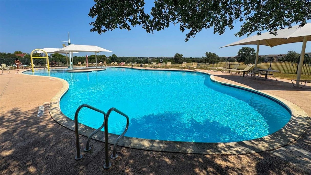 A swimming pool with a curved edge, surrounded by lounge chairs and umbrellas.
