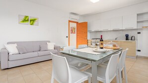 A modern kitchen with white cabinets, a dining table with chairs, and a sofa in a living area. - Holiday Apartment "Villa Marconi 5" with Sea View, Covered Terrace & Large Garden (Golfo Aranci)