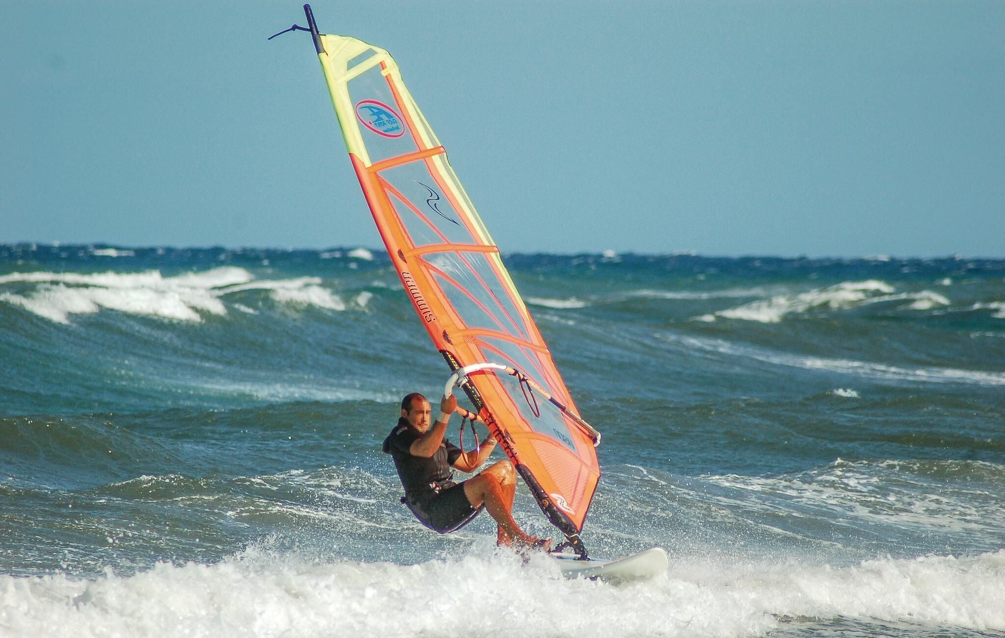Eine Person windsurft mit einem farbenfrohen Segel an einem Surfbrett im Meer.