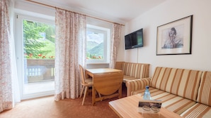 A room with a wooden desk, a striped sofa, a television, and a window with curtains.