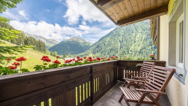 A balcony with wooden railings, a wooden bench, and a view of mountains.