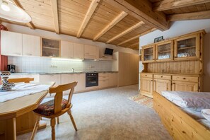 A kitchen with wooden cabinets, a dining table with chairs, a built-in oven, and a television mounted on the wall.