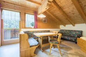 Ein Holzhütten-Interieur mit Esstisch, Bank, Sofa und einem Fenster mit Vorhängen.