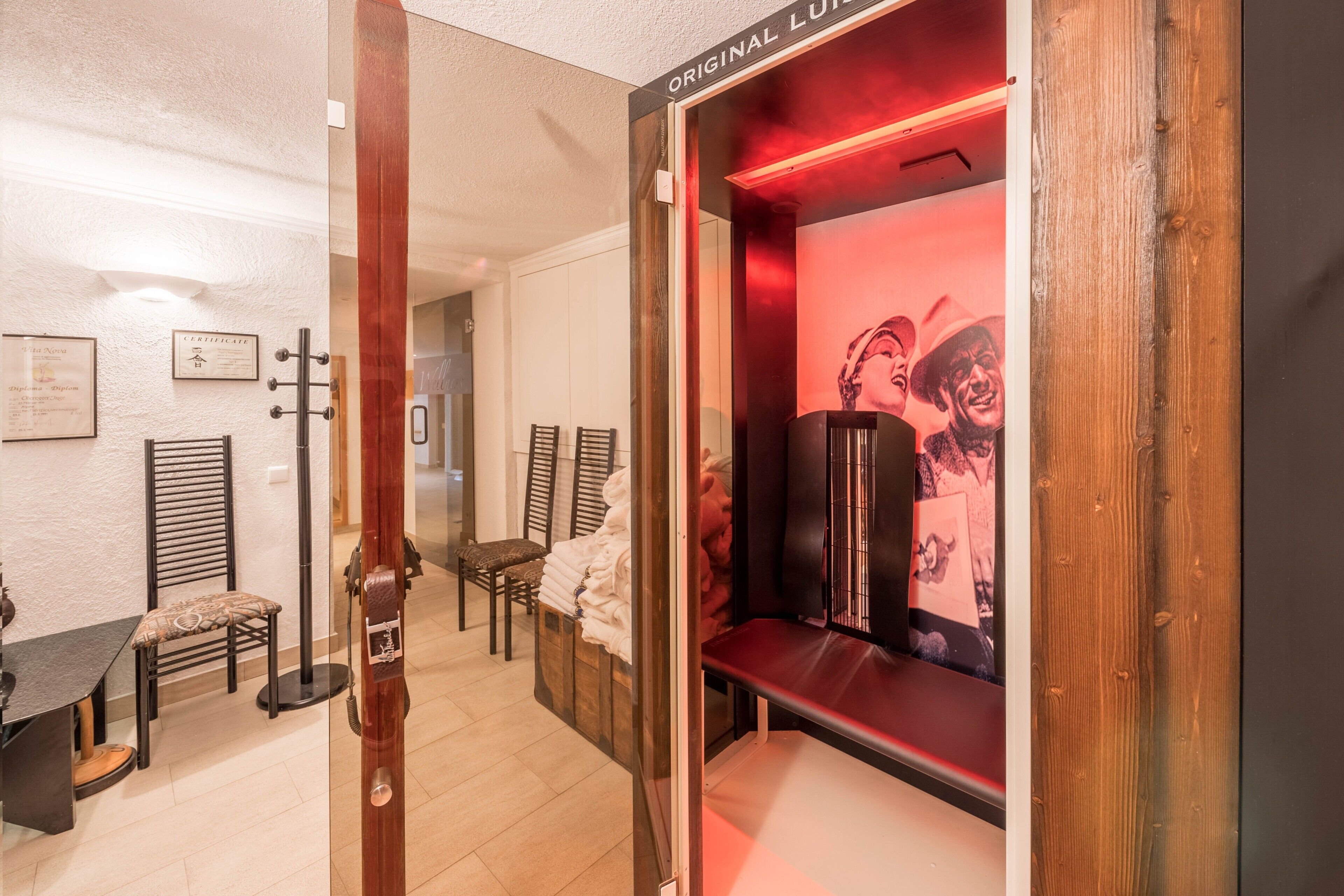 Une pièce avec une porte en bois portant l’inscription « ORIGINAL LUN », un mur éclairé en rouge avec une affiche, un banc en bois et une table avec des chaises.