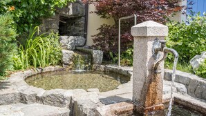 A stone fountain with water flowing, surrounded by rocks and greenery. - Cozy Apartment "Haus Hubertus - 6" with Mountain View & Wi-Fi (Walten)