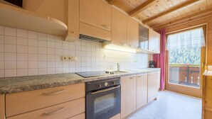 A kitchen with wooden cabinets, a stove, and a window with a view of trees. - Cozy Apartment "Haus Hubertus - 6" with Mountain View & Wi-Fi (Walten)
