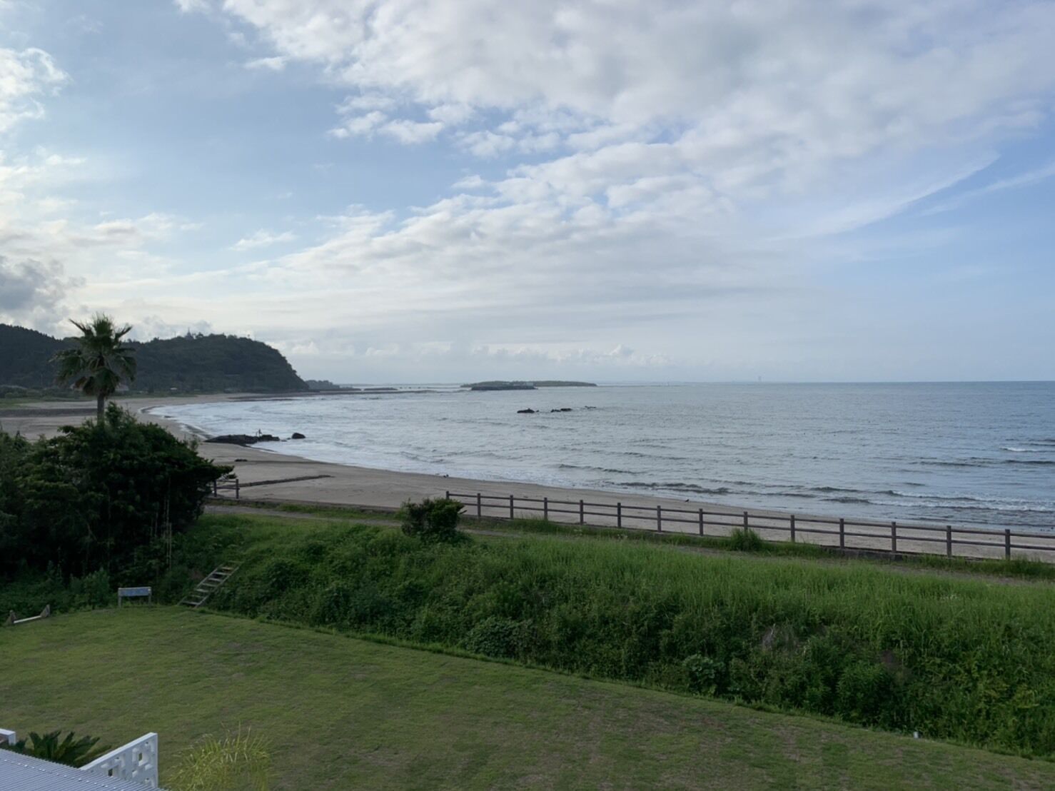 A coastal view with a beach, a wooden fence, and a grassy area.