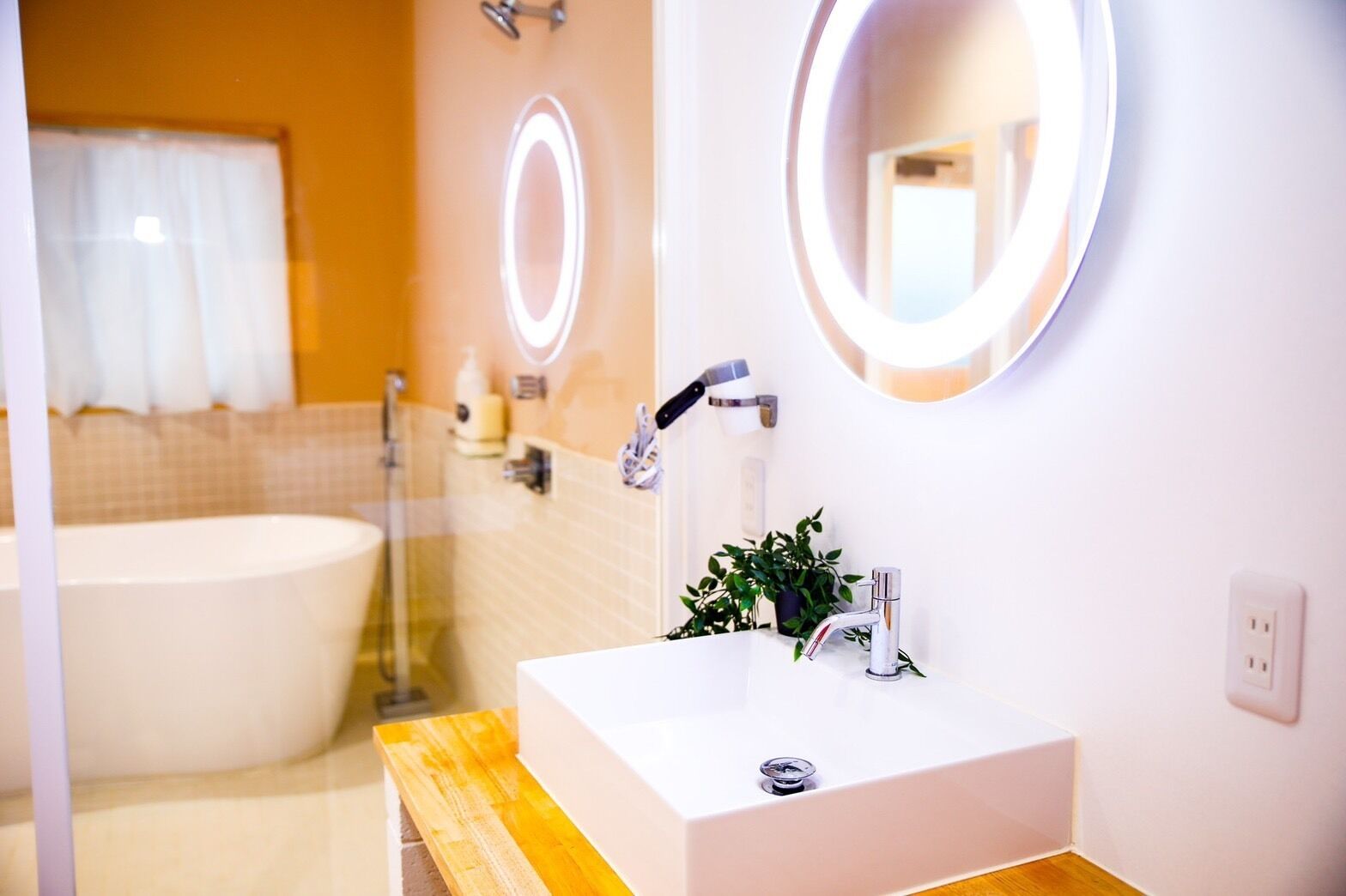 A modern bathroom with a large bathtub, a white sink with a mirror, and a wooden vanity.