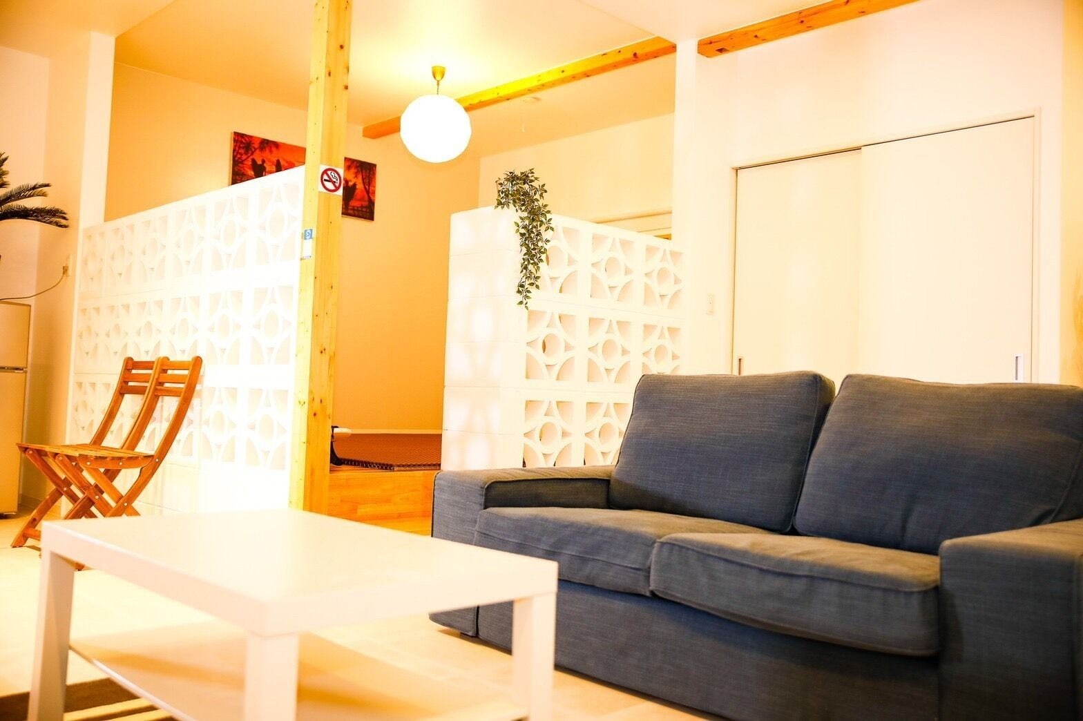 A living room with a grey sofa, a white coffee table, a wooden chair, and a white partition with a geometric pattern.