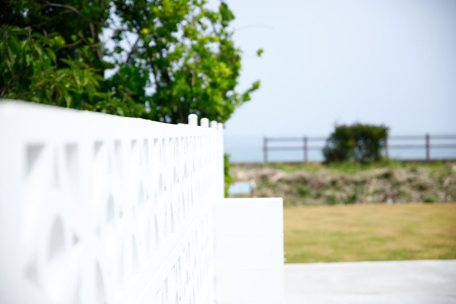 Una cerca blanca con diseño decorativo, un área con césped y un muro de piedra al fondo.