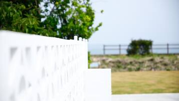 Una cerca blanca con diseño decorativo, un área con césped y un muro de piedra al fondo.