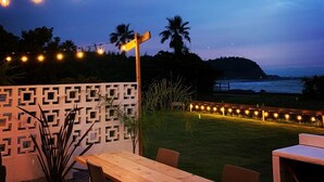 An outdoor patio area with string lights, a wooden table, chairs, and a decorative fence. - Shirahama Beach Garden (Miyazaki)