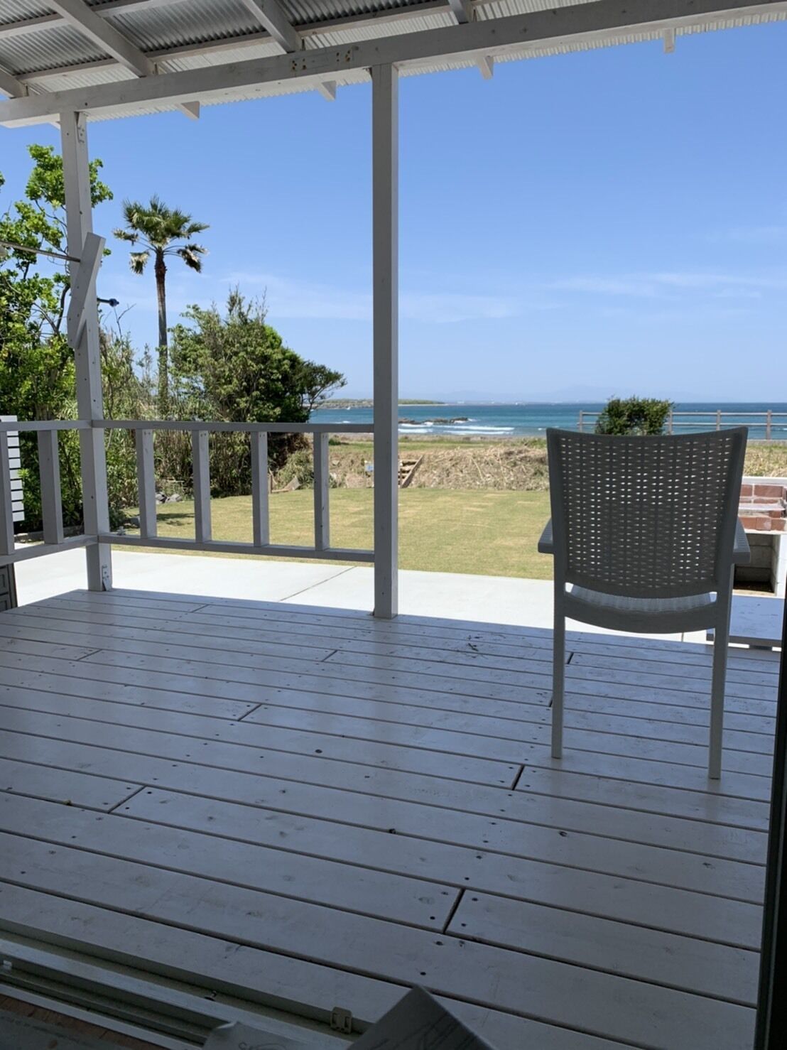 Un espacio al aire libre techado con un piso de madera, una silla de metal y vista al océano.