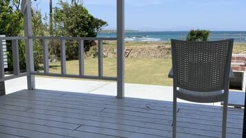 Un espacio al aire libre techado con un piso de madera, una silla de metal y vista al océano.