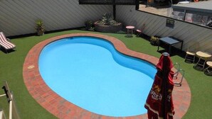 Une piscine bordée de briques, entourée de pelouse et agrémentée de quelques plantes en pot.