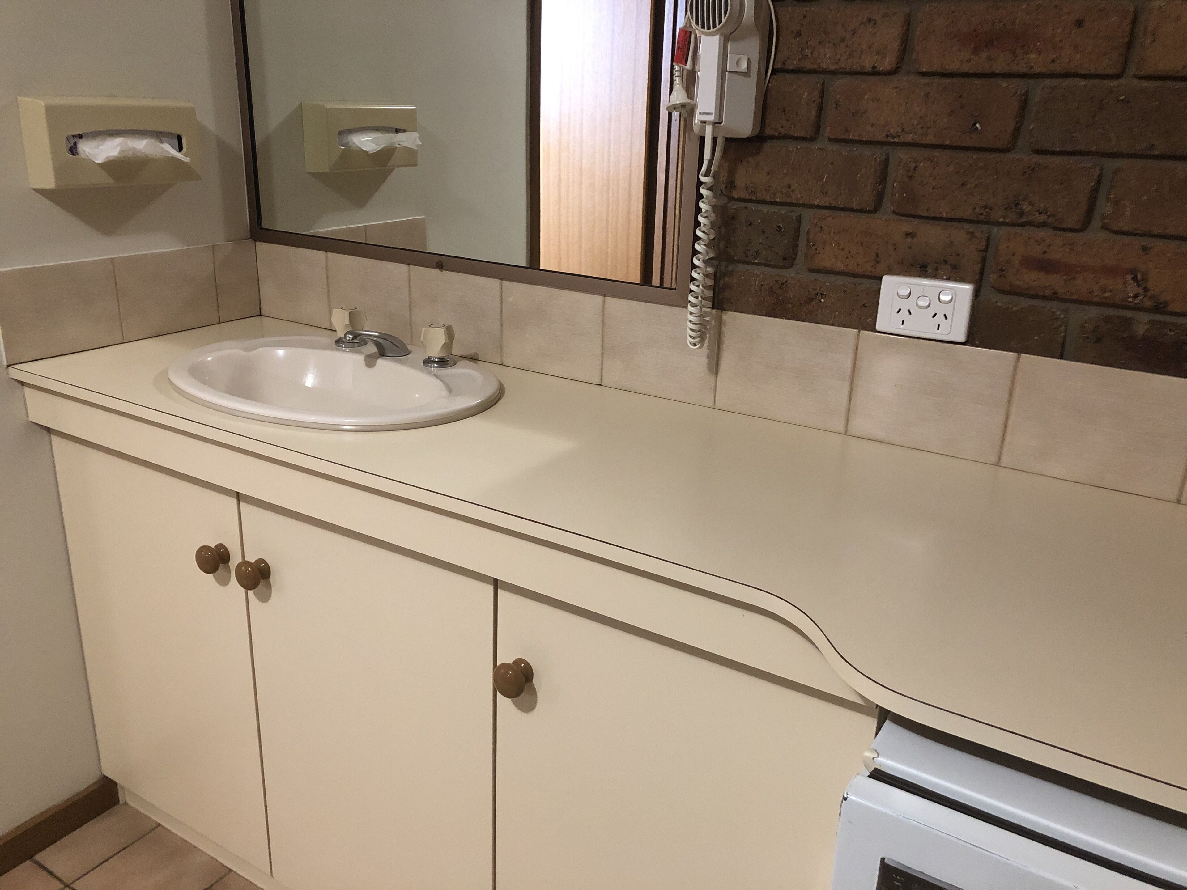 Un baño con lavamanos, espejo y secador de pelo fijado a la pared.