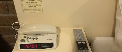 A white bedside table with a white clock displaying 10:57, a white Venturer phone, and a white remote control.