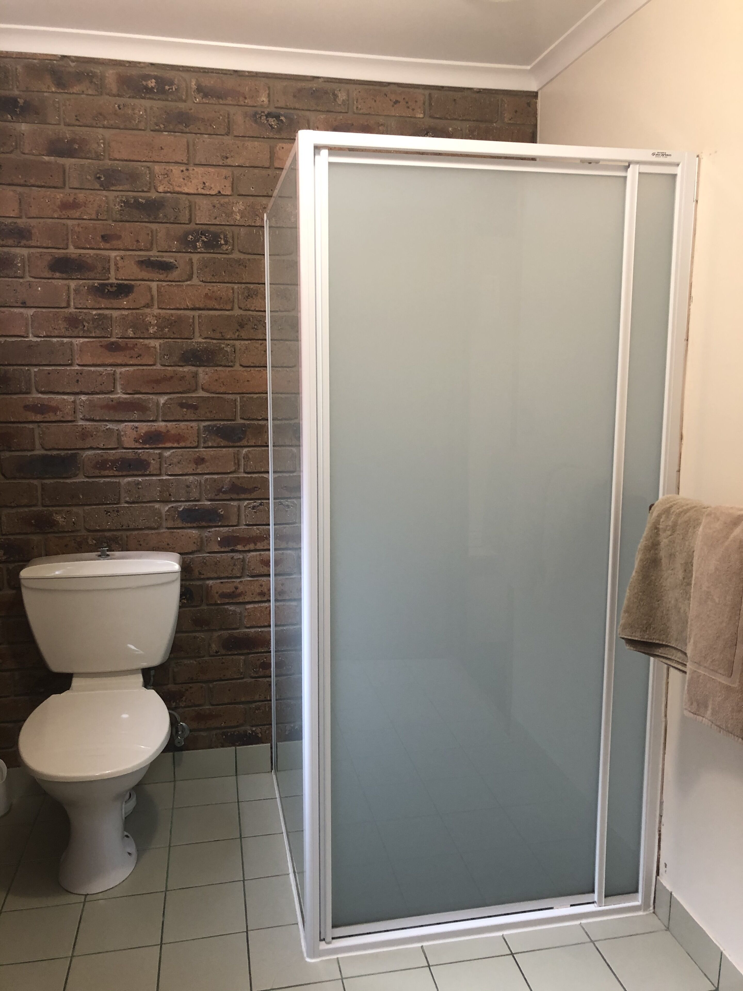 Een badkamer met een douchecabine van glas, een toilet en een handdoek aan de muur.
