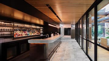 A modern bar with a long counter, shelves of bottles, and glasses.