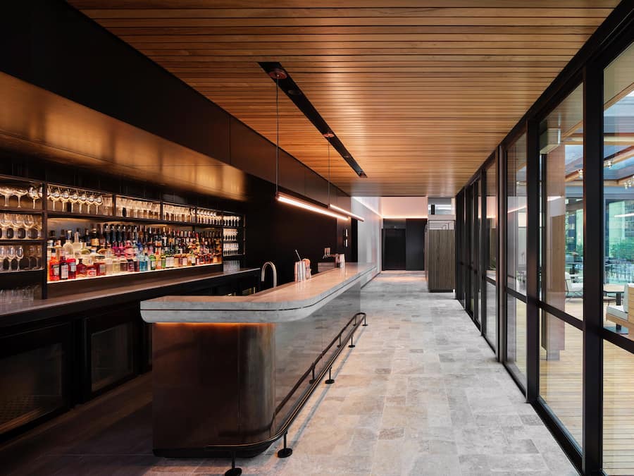 A modern bar with a long counter, shelves of bottles, and glasses.
