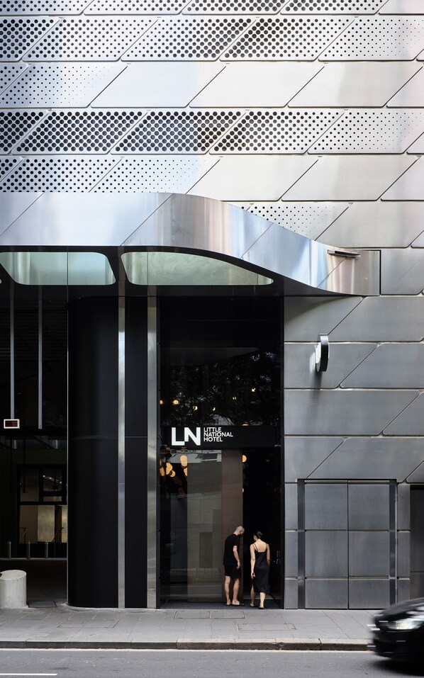 A modern hotel entrance with a curved glass facade and a metallic exterior.