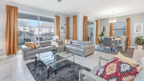 Un salon moderne avec un canapé gris, une table basse en verre et un coin repas comprenant une table et des chaises.