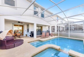 Una zona de piscina con una estructura de vidrio, un espacio de estar con un sofá cubierto, y una zona de barbacoa.