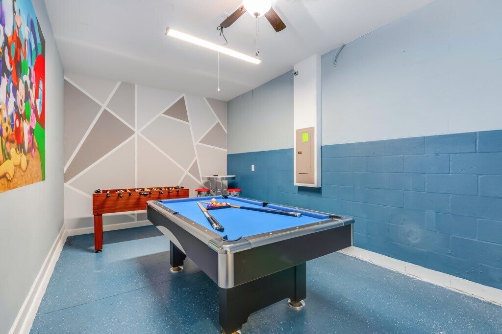 A pool table in a room with a blue and white color scheme, a ceiling fan, and a wall-mounted light fixture.