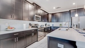 Une cuisine moderne avec des meubles de couleur sombre, des appareils électroménagers en acier inoxydable et un grand îlot central.