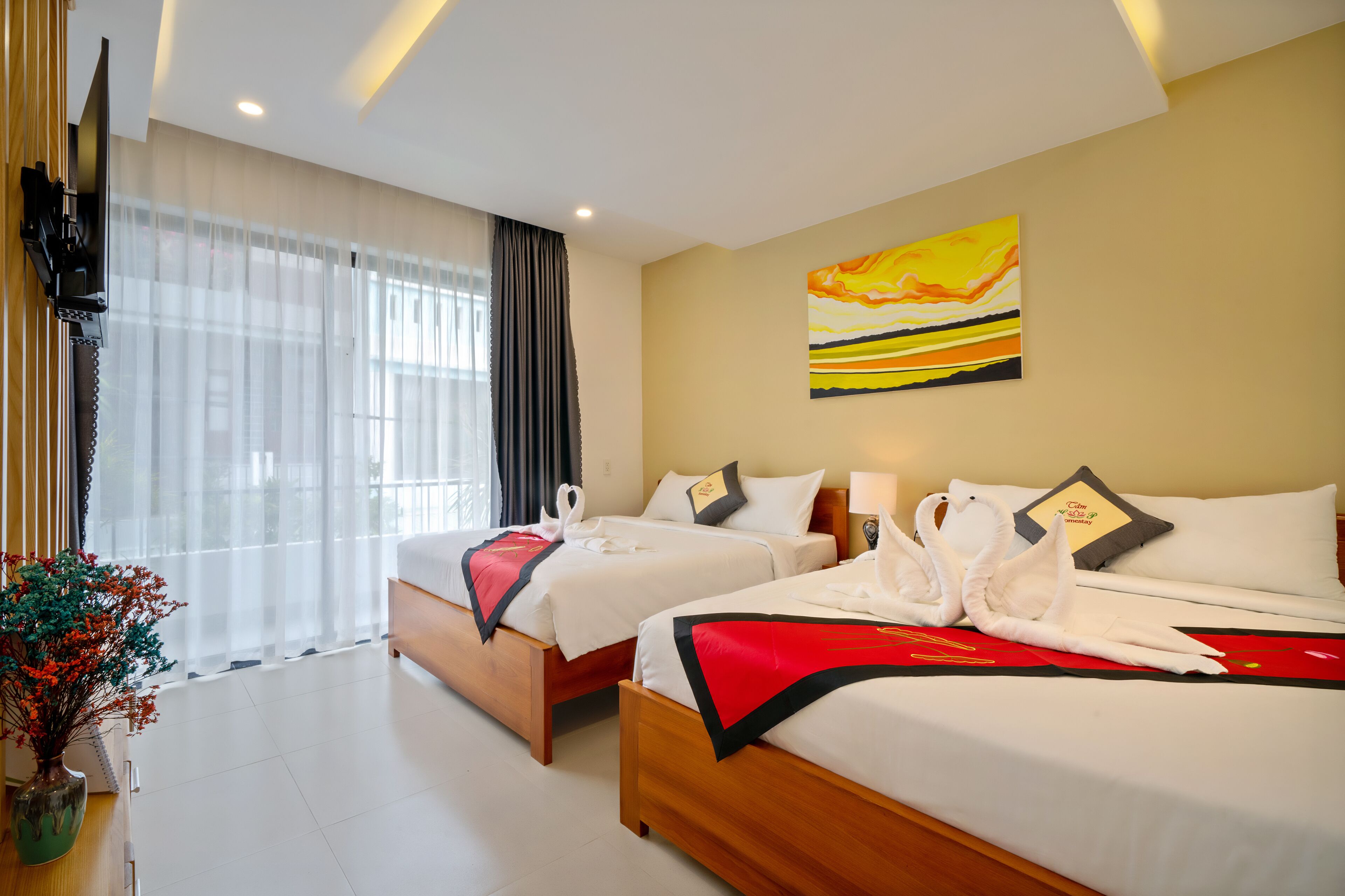 A hotel room with two beds, a painting on the wall, a TV mounted on the wall, and a window with curtains.
