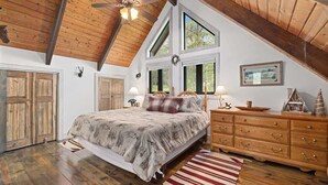 A bedroom with a large bed, wooden dresser, and a sloped ceiling.